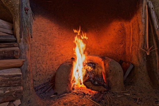 Loderndes Feuer und Holzstapel in einem Lehmhaus.