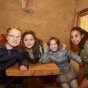 Vier Mädchen versammeln sich für das Foto um einen Holztisch in einem Lehmhaus. Sie schauen fröhlich in die Kamera.