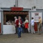 Blick auf die römsiche Taverne. Besucher stehen vor dem Tresen, der sich in einem geöffneten Tor eines weiß angestrichenen Gebäudes befindet, an.