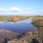 Die vollständig unter Wasser stehenden Grabungsflächen, weit im Hintergrund die Innenkippe des Tagebaus.