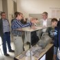 Dr. Alfred Schuler, Mitarbeiter der Außenstelle Titz, zeigt Funde des vergangenen Jahres aus dem Tagebau Garzweiler. Er und interessierte Besucher stehen vor seiner Vitrine mit Keramikgefäßen und Knochen.