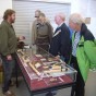Dr. Jürgen Thissen zeigt seine altsteinzeitlichen Funde und seine Experiemente mit Birkenpech, dem Klebstoff der Steinzeit. Er und Besucher stehen an seiner Vitrine im Ausstellungsraum.
