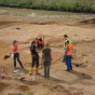 Mitarbeiter der Außenstelle Titz arbeiten mit Schaufeln auf der Grabungsfläche. Im Hintergrund noch ein überschwemmter Bereich.