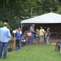 Foto: Kinder stehen vor einem Zelt, unter dem die Fläche der Kinderausgrabung liegt. Seitlich stehen Tische mit Kisten und eine Schubkarre.