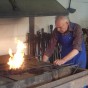 Foto: Blick in die Schmiede. Herr Lessenich hält ein Werkstück mit einer Zange ins Schmiedefeuer.