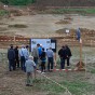 Foto: Blick über die Grabungsfläche mit Besuchern. Im Hintergrund befindet sich die Kippe und zwei Braunkohlekraftwerke. Links im Bild steht ein Bagger.