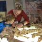Auf einem beleuchteten Tisch liegen Pferdeknochen, eines fast vollstädigen Skeletts. Eine Frau zeigt einem Jungen mit blauer Jacke die Zähne des Tierschädels. Im Hintergrund stehen Stellwände mit Postern.