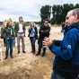 Besucher stehen vor einer Posterstellwand und lassen sich von einer weiteren in blauer jacke etwas erklären. Im Hintergrund weitere Besucher und Pappeln.