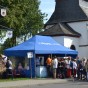 Vor einer Kapelle steht ein blaues Zelt, davor eine Schlange anstehender Personen.