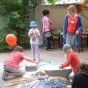 Vor einem großen Zelt werden Luftballons aufgeblasen und Kinder mahlen Getreide mit Handmühlen.