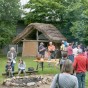 Vor Lehmhäusern mit Strohdach befinden sich Besucher.