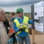 Ein Archäologe in Warnweste und Helm deutet auf ein Poster , ein Besucher schaut zu.