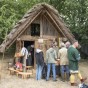 Personen stehen vor einem Strohgedeckten Holzhaus.