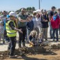 Eine große Besuchergruppe aus Ewachsenen und Kindern steht bei einem Mann mit Helm und Warnweste, der auf den Boden zeigt.